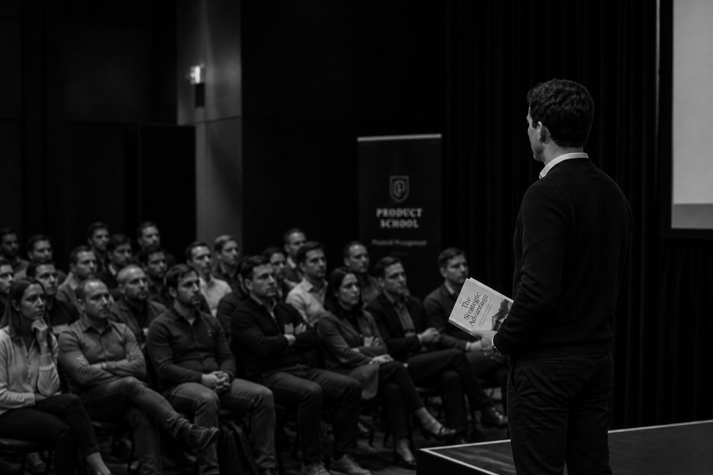 Black and white photo of a speaker presenting his book to an attentive audience at a professional conference on personal branding and strategy